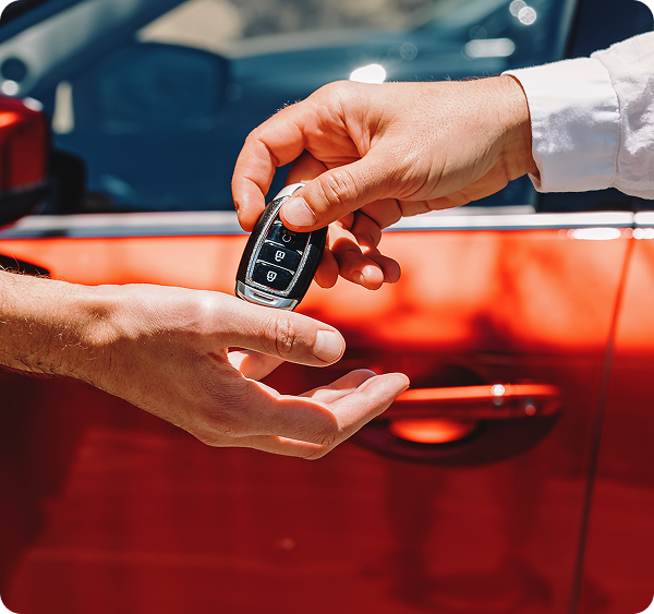 Person handing over a car key fob to another near a red car.